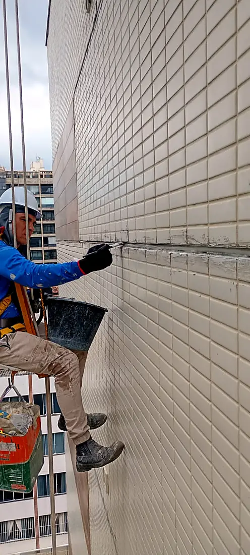 Alpinista industrial aplicando impermeabilização na junta